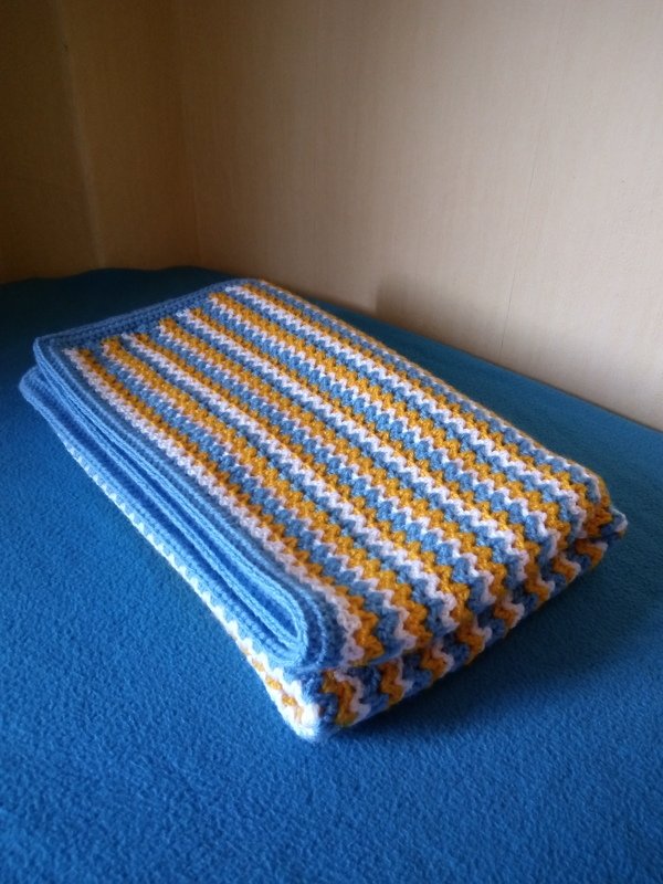 Gefaltete handgehäkelte Babydecke mit blau-weiß-gelben Streifen auf blauem Untergrund