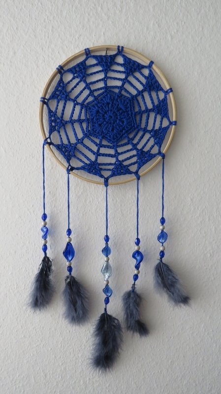 Blauer gehäkelter Traumfänger auf Holzring mit Perlen und grauen Federn an der Wand