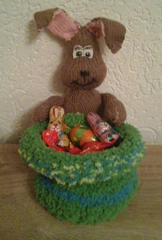 Gestrickter brauner Hase mit Schlappohren und grünem Körbchen voller Osterfiguren