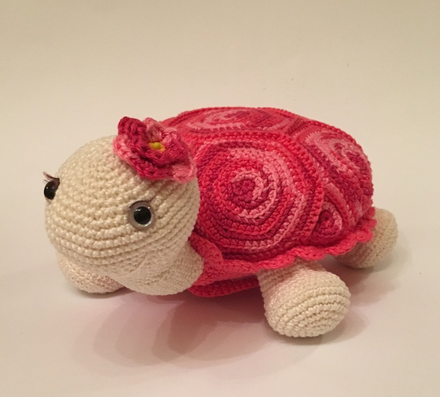 Amigurumi turtle with pink swirl shell, cream body, black safety eyes with stitched lashes and a small pink flower on the head.