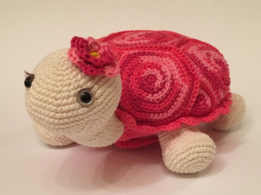 Gehäkelte Schildkröte mit rosa Spiralpanzer, cremefarbenem Körper und Häkelblüte