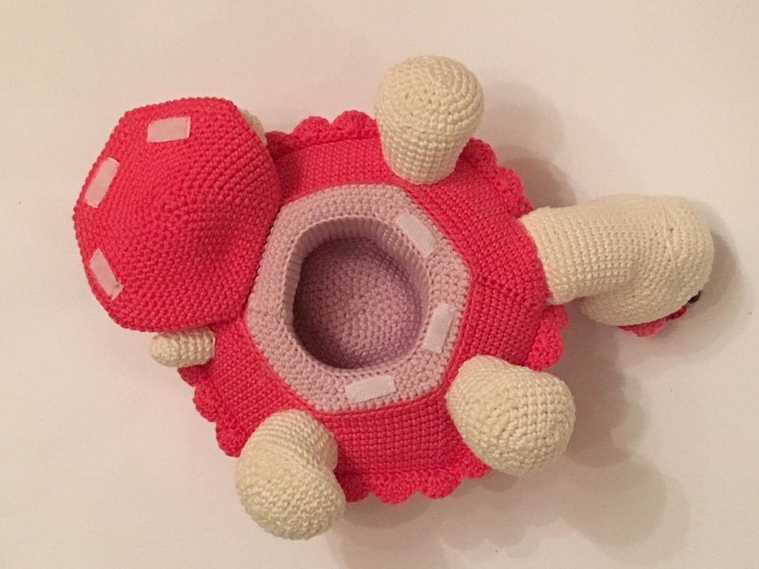 Top view of a pink and cream crocheted turtle storage amigurumi with removable shell showing hollow interior and fastening tabs