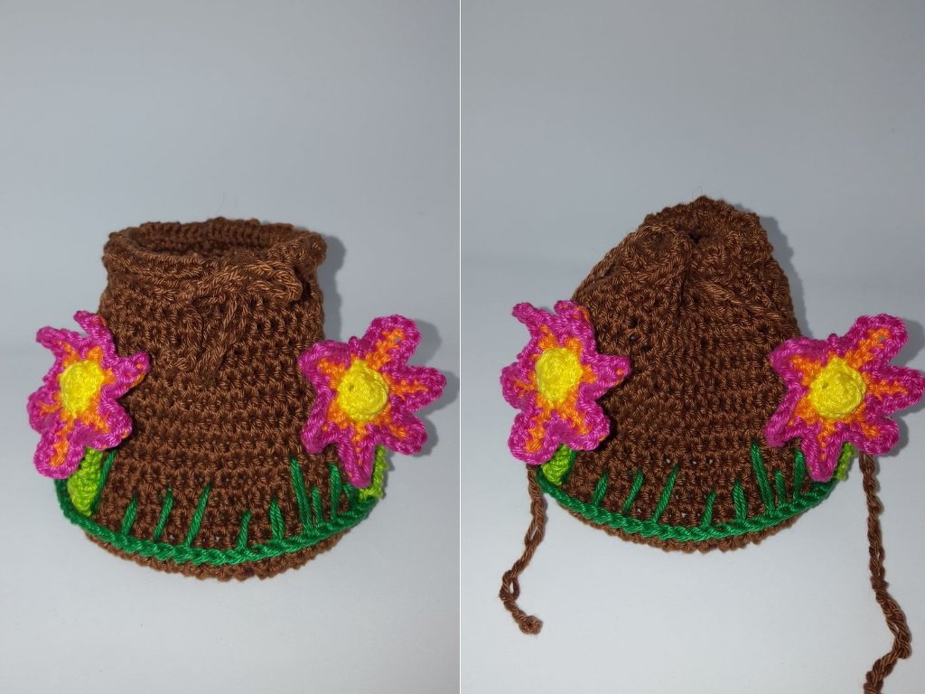 Nahaufnahme eines braunen Amigurumi-Baumstumpfs mit grüner Einfassung und pink-gelben Blumen