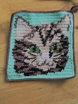 Quadratischer gehäkelter Topflappen mit Katzenkopf auf mintgrünem Hintergrund