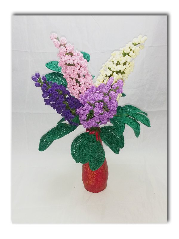 Gehäkelter Strauß mit violetten, rosa und cremefarbenen Blüten sowie großen grünen Blättern in roter Vase