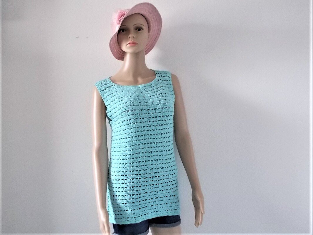 Mannequin trägt ärmelloses, gehäkeltes Damen-Top in Türkis mit durchbrochenem Muster und rosa Hut.