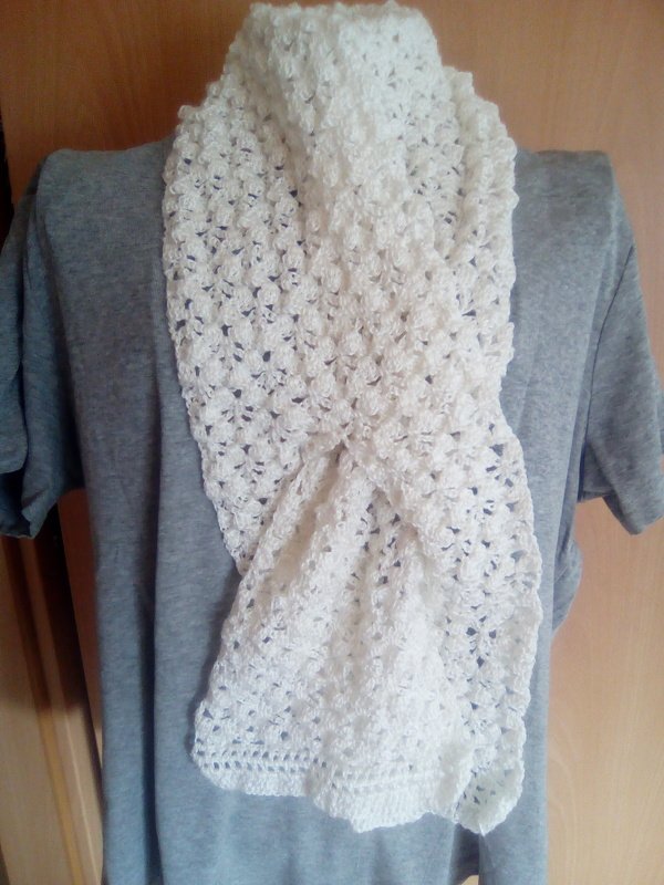 Weißer gehäkelter Schal mit wiederholtem Maschenmuster, drapiert an einer grauen Schaufensterpuppe.