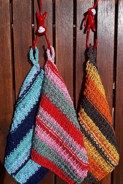 Drei gestrickte Tücher mit Streifenmustern an roten Haken vor einer Holzwand