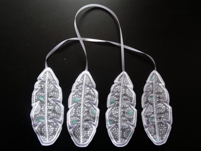 Vier bestickte Blattformen mit weißer Spitze und mintfarbenen Akzenten, verbunden durch ein schmales Band