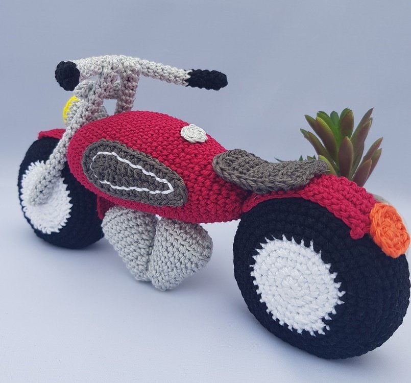 Red crocheted amigurumi motorcycle toy with black-and-white wheels and gray engine details