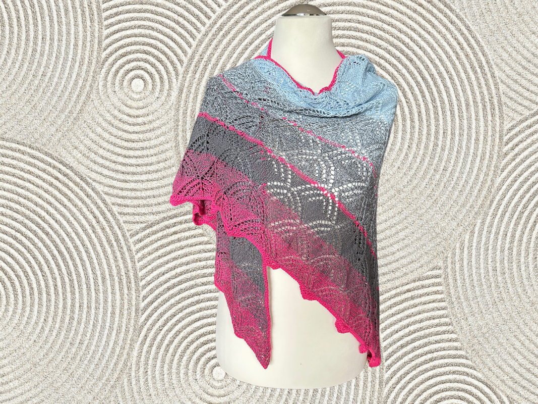 Gestricktes Dreieckstuch in Blau, Grau und Pink mit Lochmuster auf einer Schneiderpuppe vor strukturiertem Hintergrund.