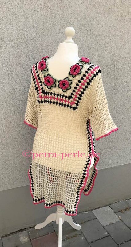Cremefarbene gehäkelte Tunika mit pinken Häkelblumen am V‑Ausschnitt und schwarz-pinken Karodetails.
