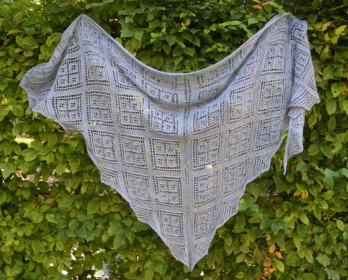Hellgraues Dreieckstuch mit quadratischem Lace-Muster vor grüner Hecke