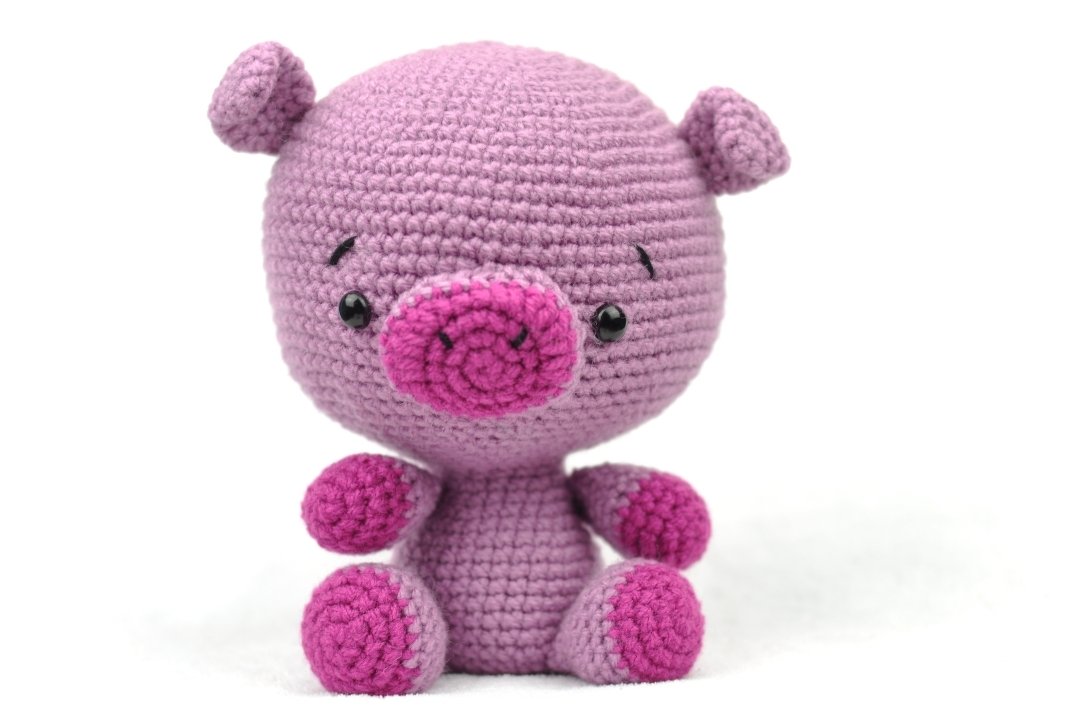 Gehäkeltes Amigurumi-Schweinchen in Lila und Pink, sitzend.