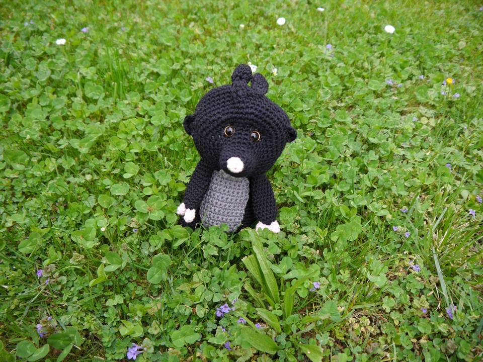 Schwarzer gehäkelter Amigurumi-Maulwurf mit grauem Bauch auf Klee