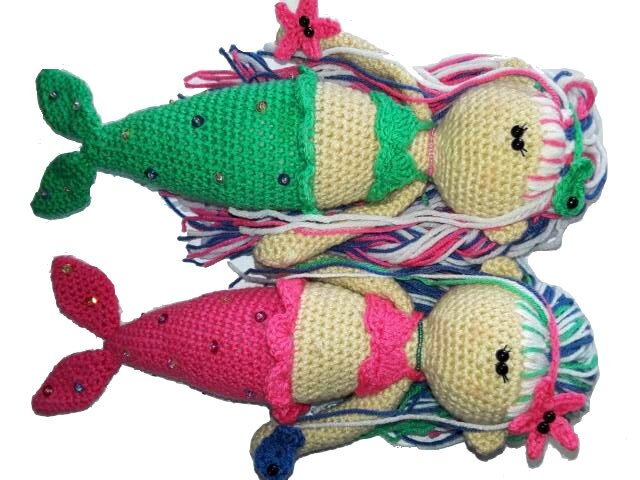 Zwei gehäkelte Meerjungfrauen-Amigurumi (grün und pink) mit mehrfarbigen Garnhaaren und Perlenakzenten auf weißem Hintergrund.