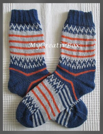 Gestrickte Socken in Blau, Grau und Orange mit Streifen- und Zickzackmuster auf hellem Untergrund