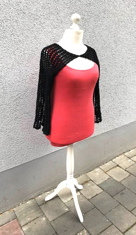 Schaufensterpuppe mit schwarzem gehäkeltem Bolero über rotem Top vor grauer Wand