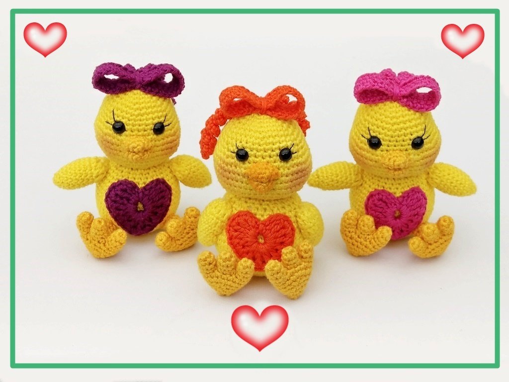 Drei gelbe Amigurumi-Küken mit violetter, oranger und pinker Schleife und passenden Häkelherzen auf weißem Hintergrund