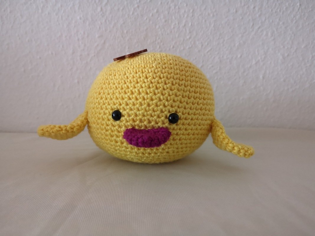 Rundes gelbes Amigurumi-Küken mit schwarzen Augen und pinkem Mund