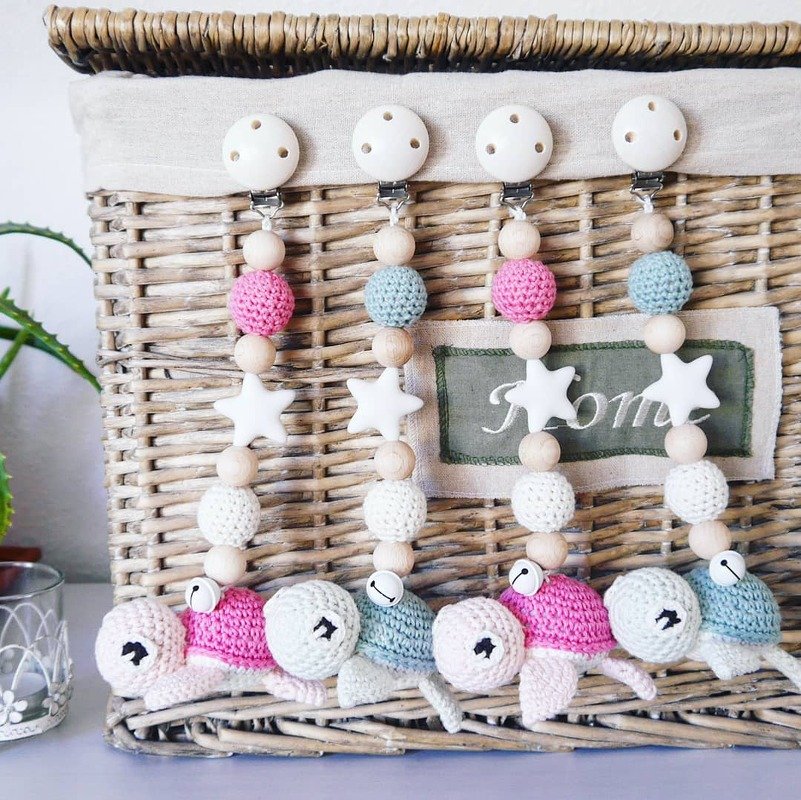 Vier gehäkelte Schnullerketten mit Schildkröten, Holzperlen, Sternen und Clips an einem geflochtenen Korb
