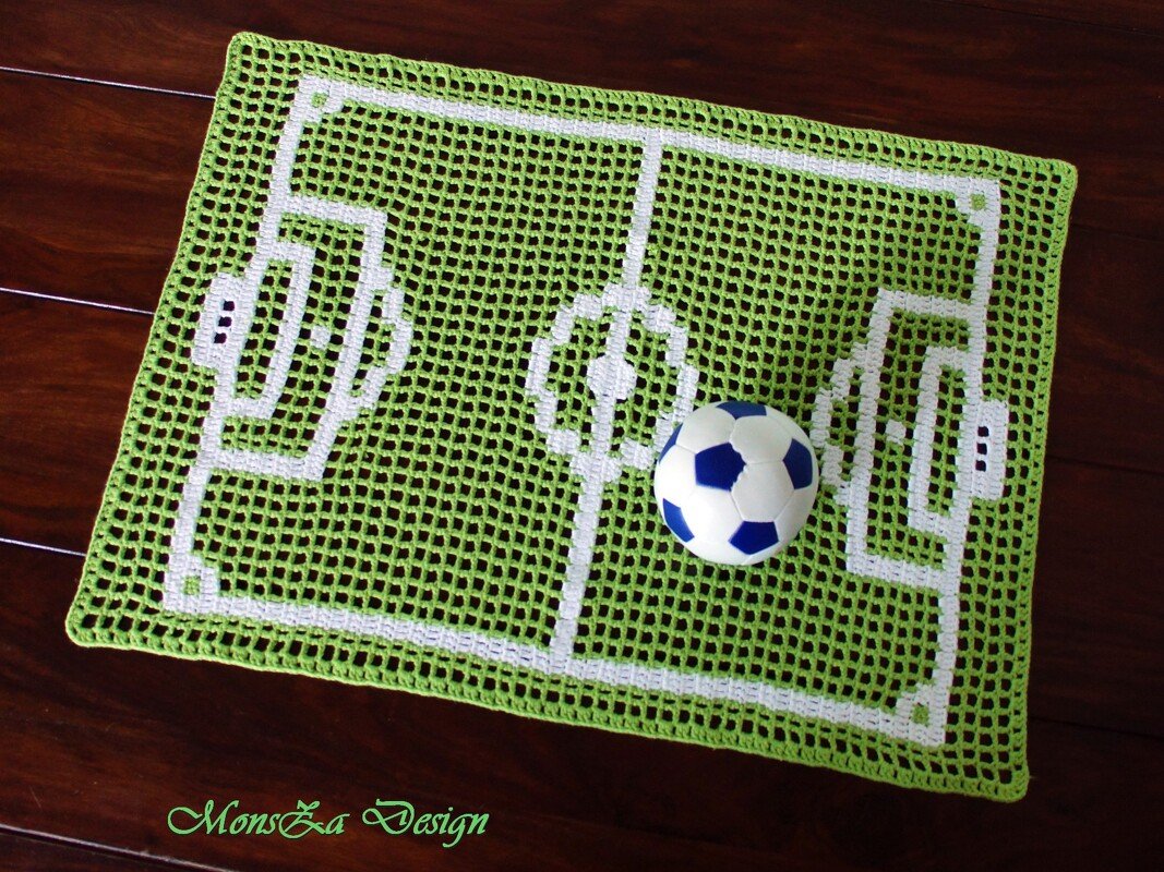 Rechteckiges gehäkeltes Deckchen in Grün mit weißen Markierungen eines Fußballfeldes und einem blau-weißen Ball