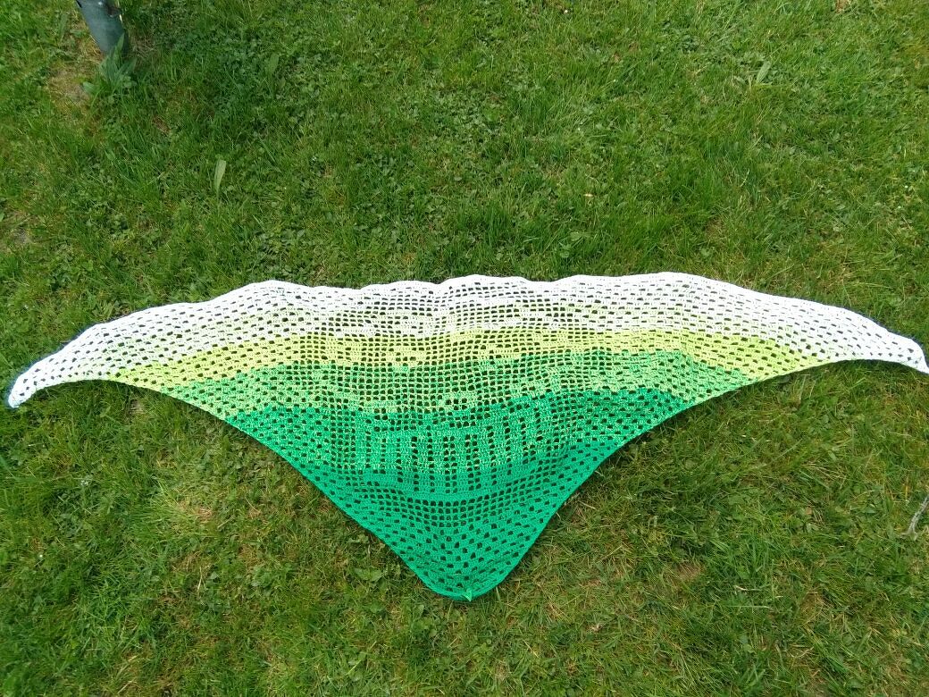 Weiß‑grünes gehäkeltes Dreieckstuch mit HELLO‑Schriftzug auf Gras.