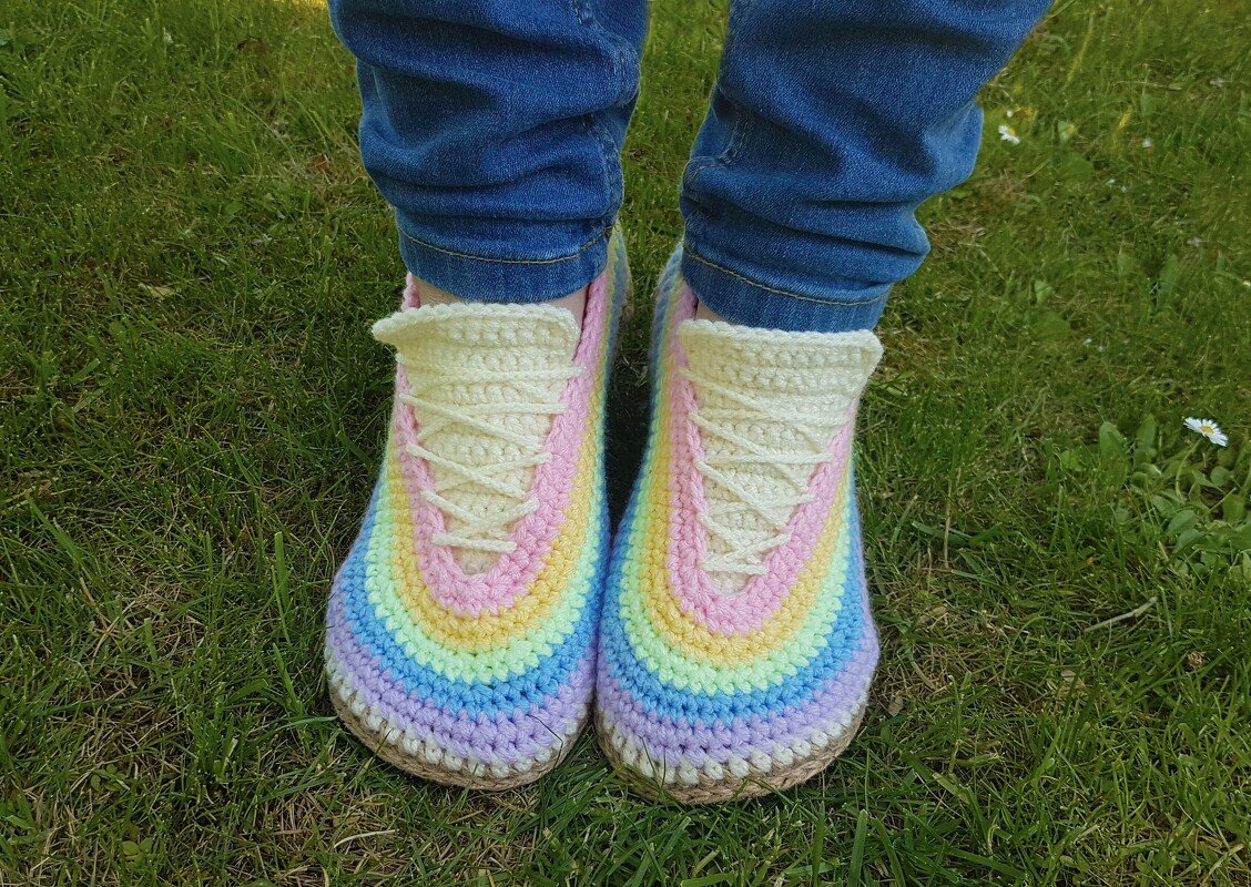 Top view of pastel rainbow crochet lace-up slippers worn with rolled jeans on grass