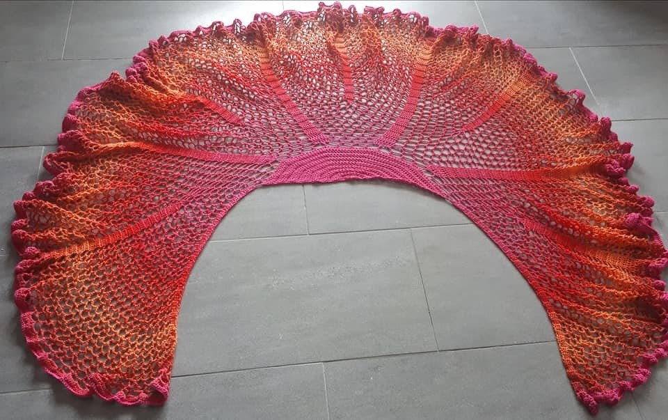 Gehäkeltes Halbrundtuch mit Farbverlauf von Pink zu Rot und Orange auf grauem Boden