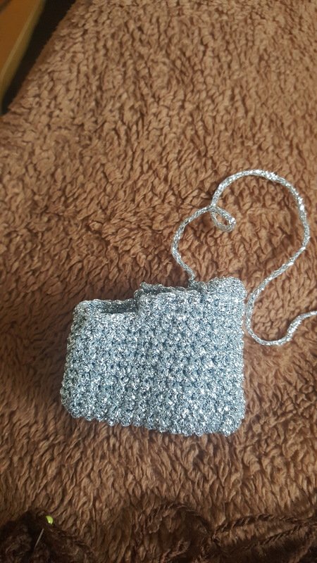 Kleine silberne, gehäkelte Tasche mit Trageriemen auf braunem Untergrund