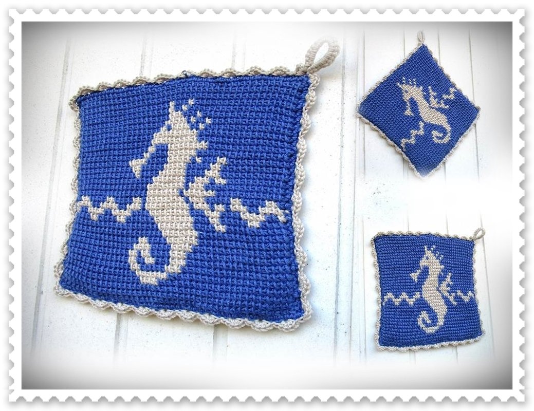 Drei blaue gehäkelte Topflappen mit beigem Seepferdchen- und Wellenmuster, ein größeres und zwei kleinere, auf hellem Untergrund.