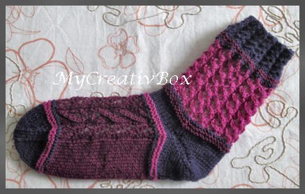 Gestrickte Socke in Dunkellila und Magenta mit Zopf- und Ajourmuster