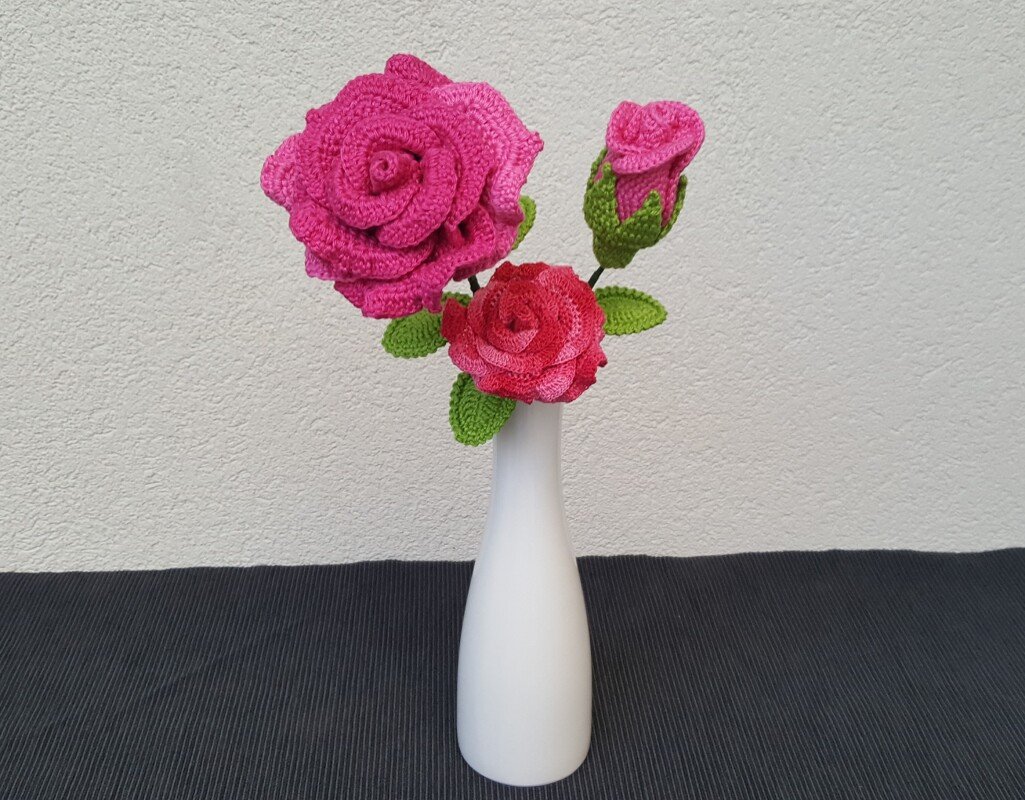 Drei gehäkelte Rosenstiele in weißer Vase mit deutlich sichtbaren Blütenlagen, Knospe und grünen Blättern