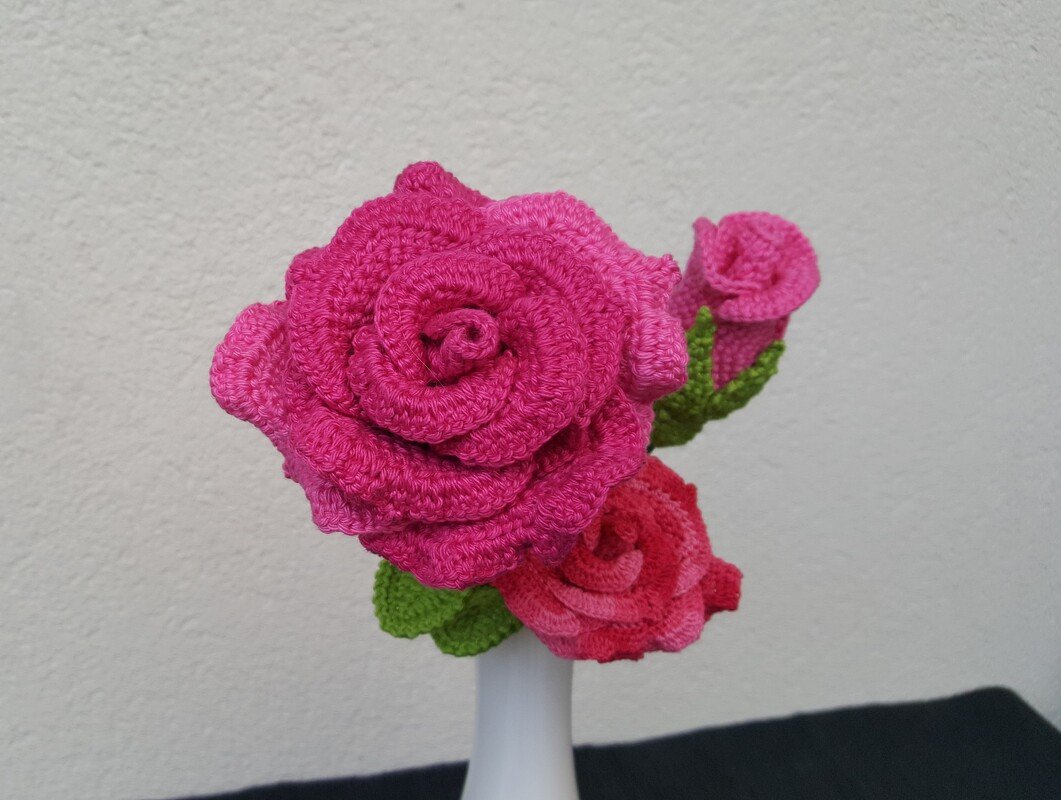 Gehäkelte pinke Rosen mit grünen Blättern in weißer Vase