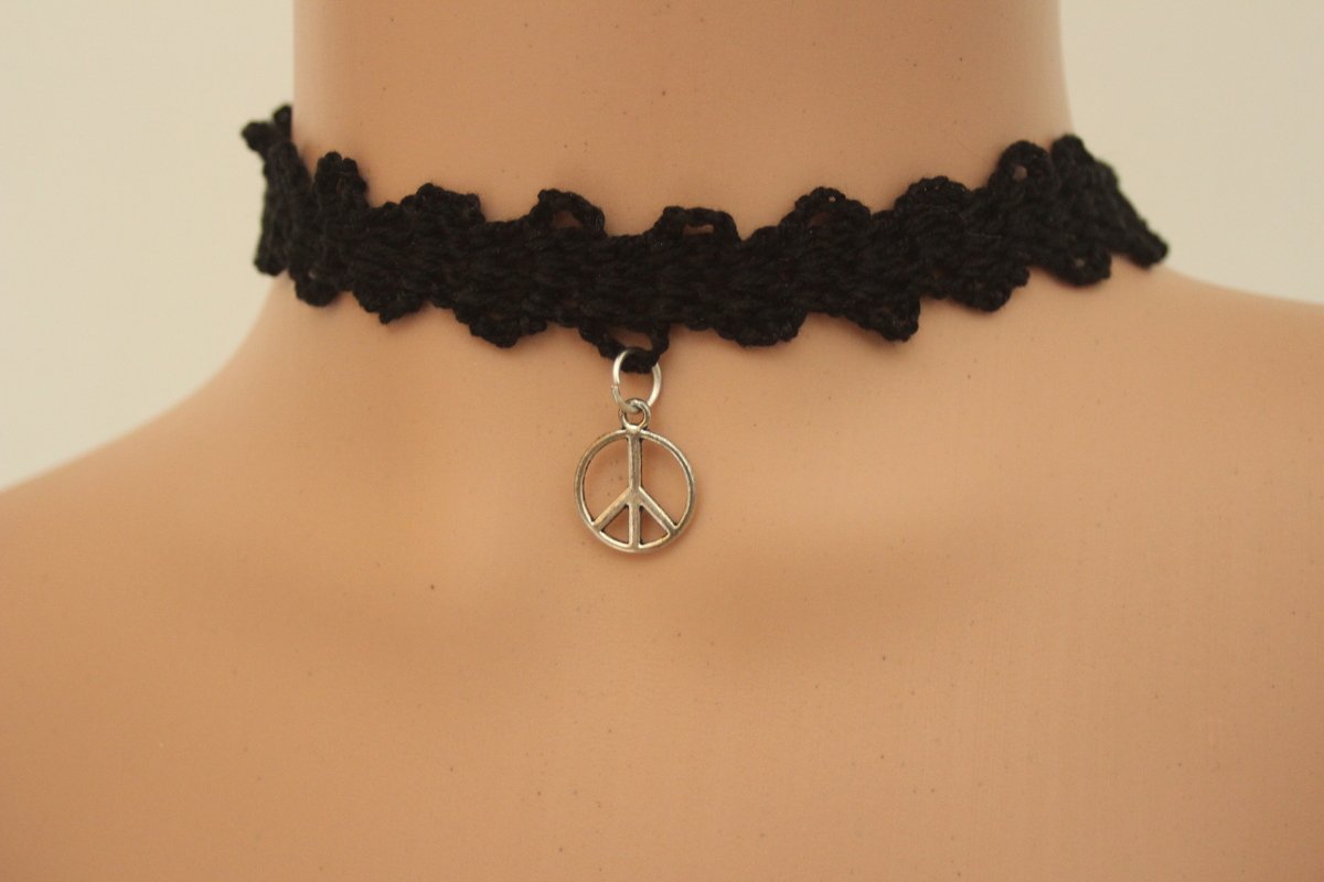 Gehäkelter schwarzer Choker mit gewelltem Rand und silberfarbenem Peace-Anhänger, am Hals getragen.