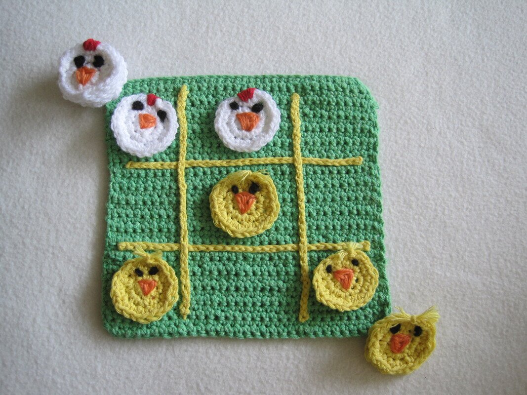 Grünes gehäkeltes Tic‑Tac‑Toe‑Brett mit gelbem Gitter und runden Küken- und Hühner-Spielsteinen