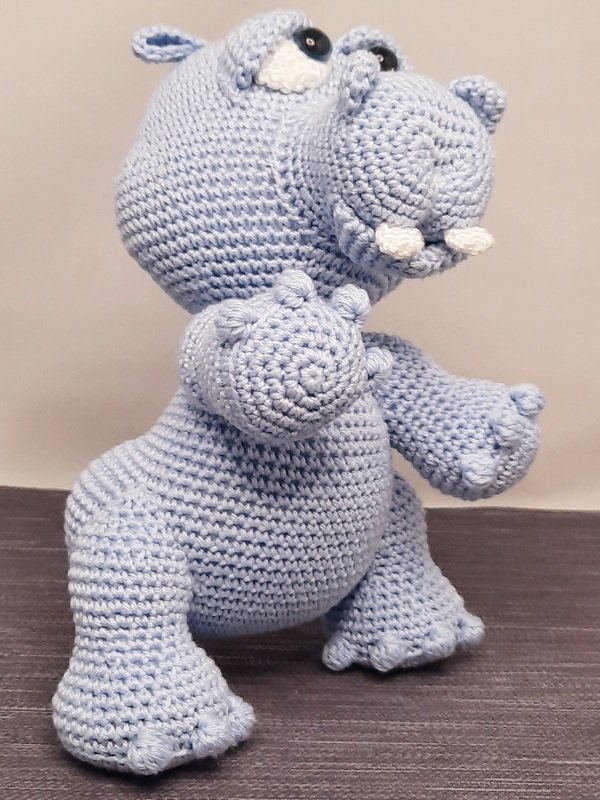 Hellblaues gehäkeltes Amigurumi-Nilpferd mit schwarzen Knopfaugen und weißen Stoßzähnen