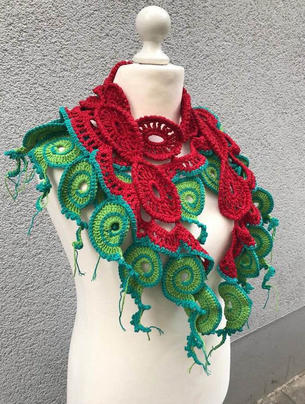 Bunter gehäkelter Schal mit roten runden Motiven und grünen Spiralmustern auf einer Schneiderpuppe
