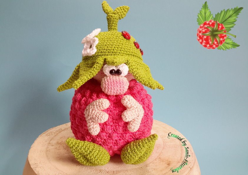 Gehäkelter Amigurumi-Wichtel in Himbeerform mit grünem Hut, weißen Blüten und roten Marienkäfern
