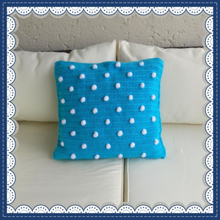 Türkises gehäkeltes Kissen mit weißen Noppen auf hellem Sofa