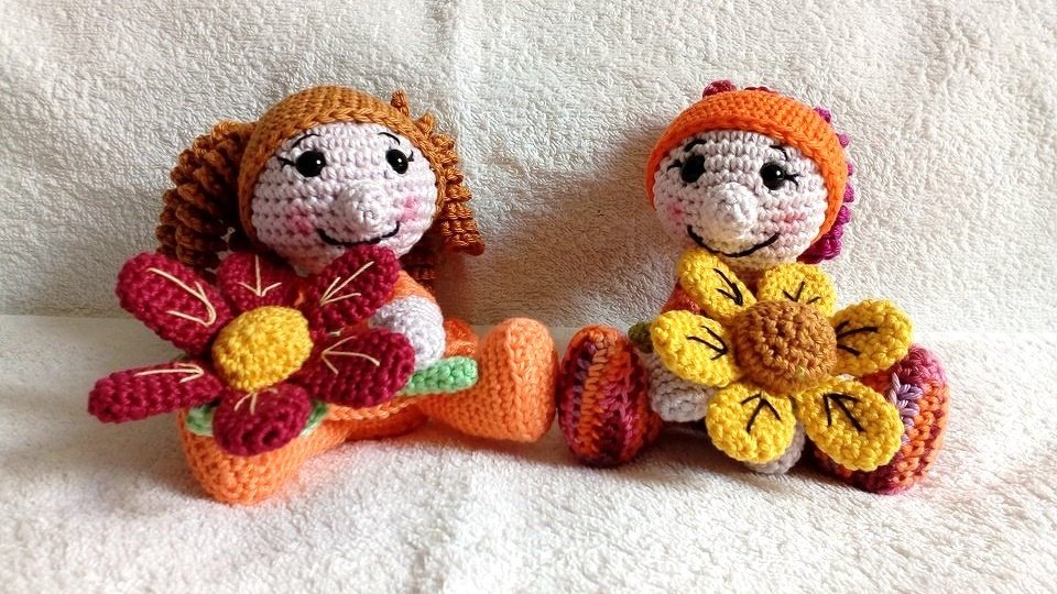 Zwei gehäkelte Amigurumi-Puppen in Orange und Gelb mit großen Blüten
