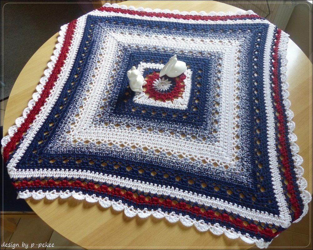 Quadratisches gehäkeltes Deckchen in Rot, Weiß und Blau mit Spitzenrand auf einem Holztisch