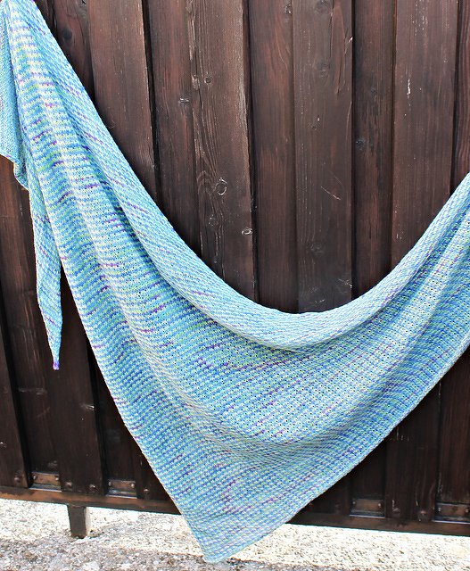 Hellblaues gestricktes Dreieckstuch mit dezenten Sprenkeln an einem Holzzaun drapiert