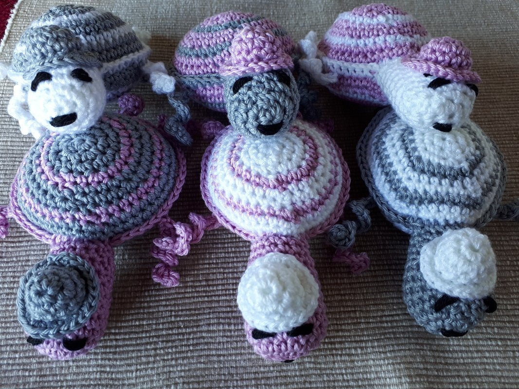Drei gehäkelte Babyspielzeug-Figuren in Rosa, Grau und Weiß mit Spiralmuster