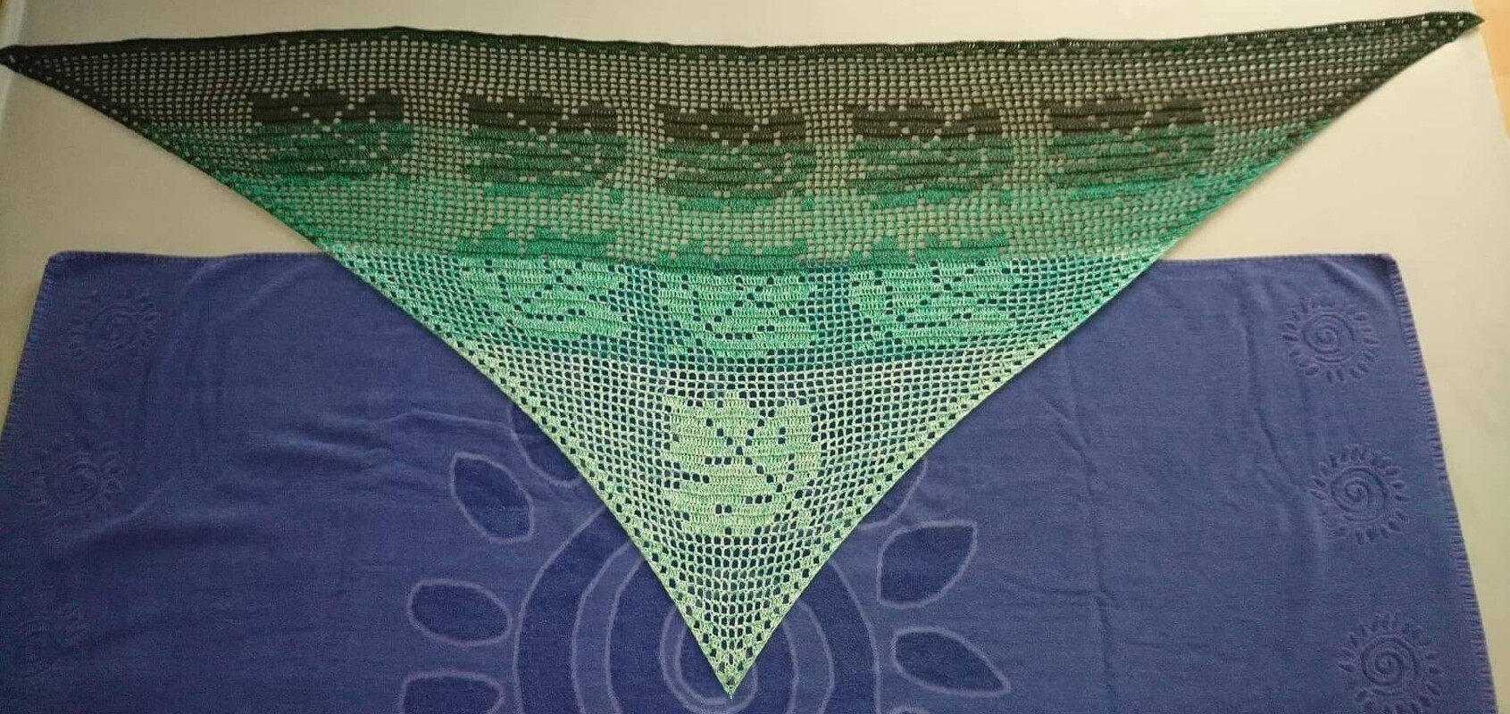 Dreieckiges Filet-Häkeltuch mit Blattmotiven und grün-schwarzem Farbverlauf, auf blauem Tuch ausgebreitet