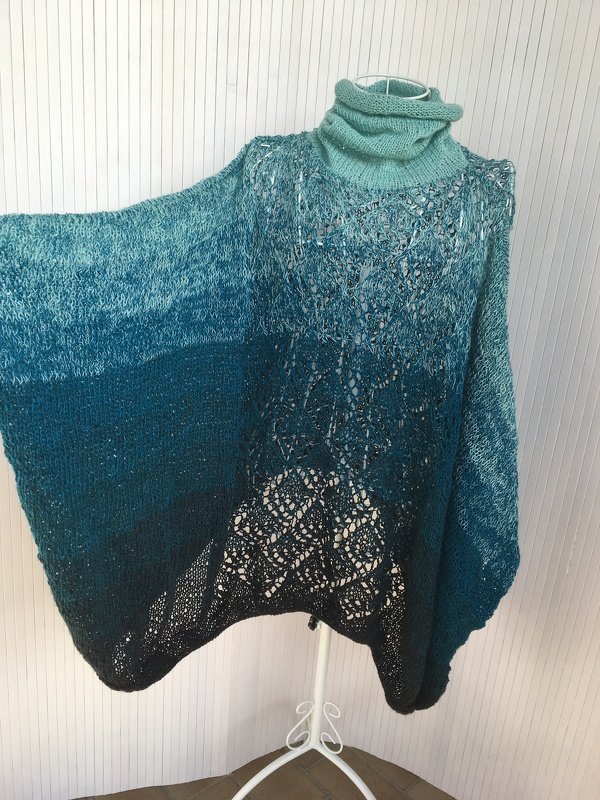Gestrickter Poncho in Türkis-Petrol Ombre mit Rollkragen und Lochmuster auf einer weißen Schneiderpuppe.