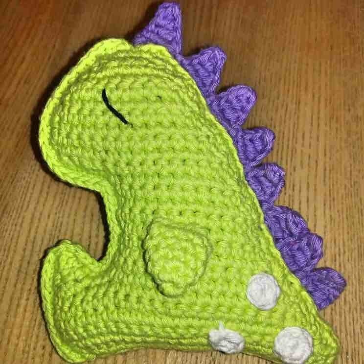 Gehäkelter grüner Dinosaurier-Amigurumi mit lila Stacheln auf Holzoberfläche
