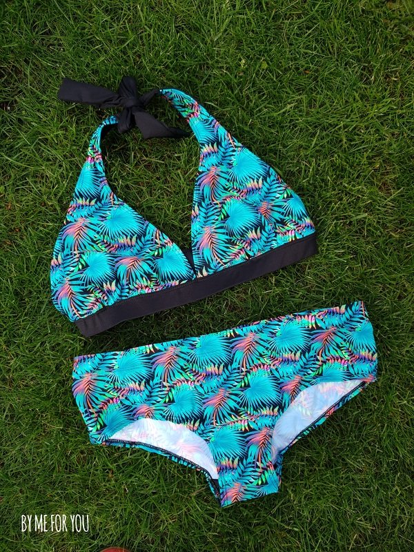 Bikini-Zweiteiler mit Neckholder-Top zum Binden und passender Bikinihose im tropischen Blattmuster in Türkis und Pink auf einer Wiese