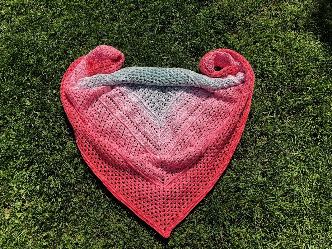 Gehäkeltes Dreieckstuch mit Farbverlauf von Grau zu Rosa und Koralle auf Gras