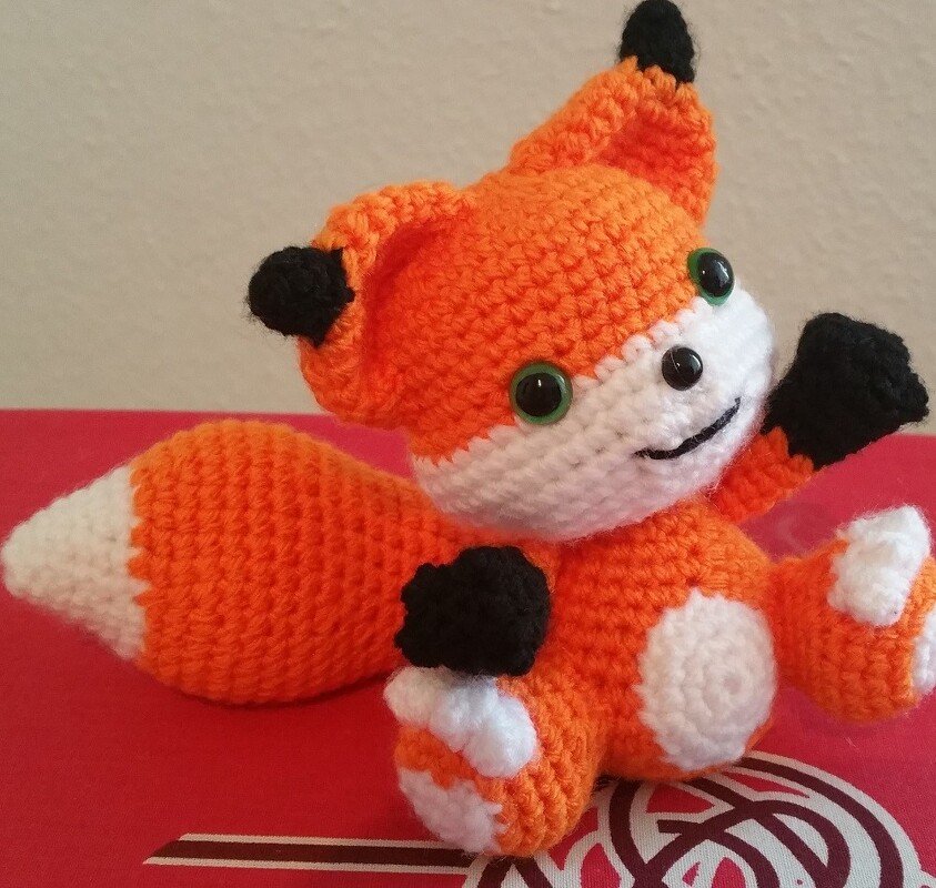 Gehäkelter Fuchs in Orange und Weiß mit schwarzen Details und grünen Sicherheitsaugen.